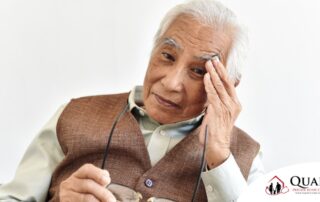 An older adult holds his head and his glasses representing vision problems like macular degeneration.